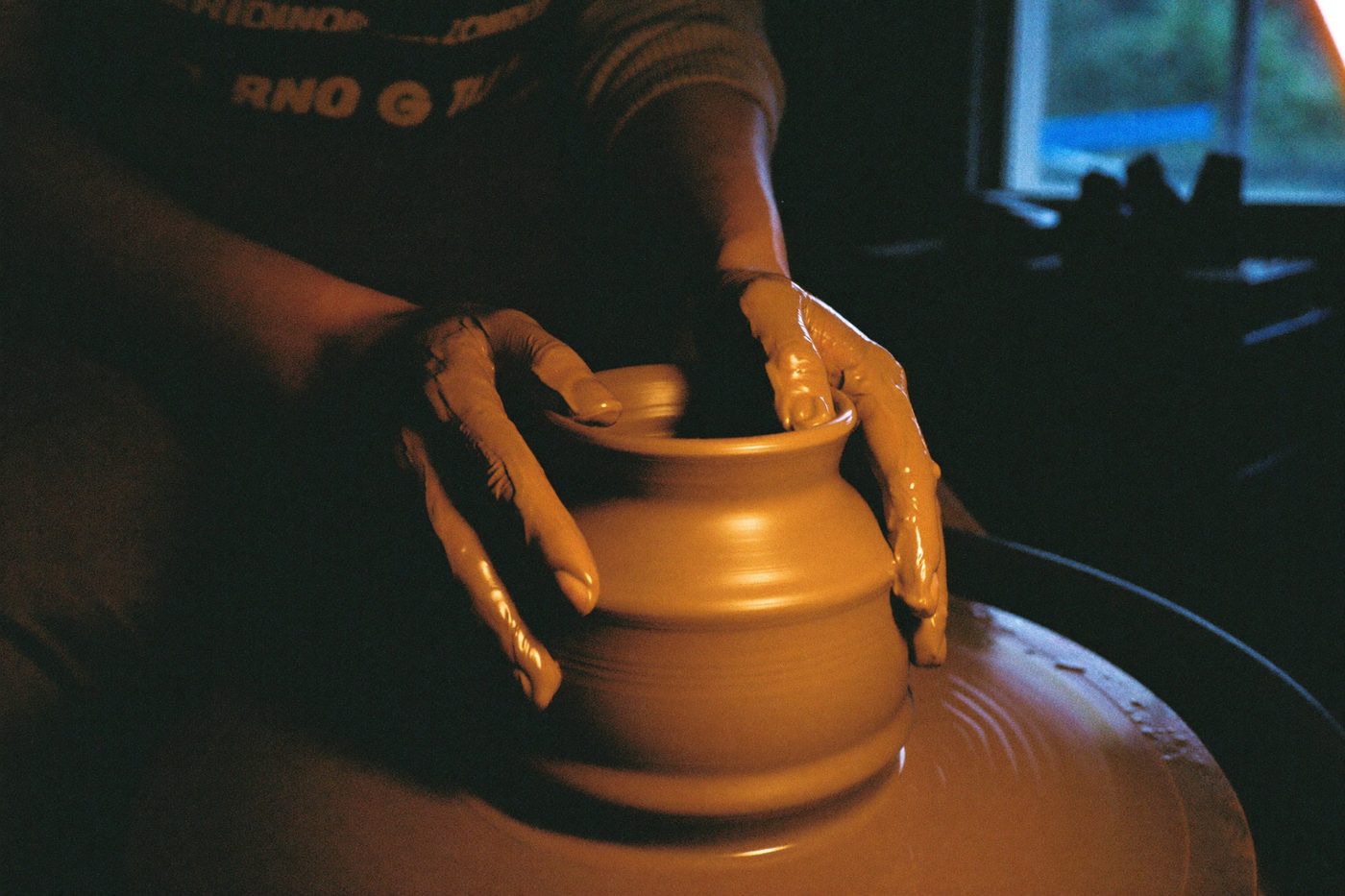 Hands centering clay on a pottery wheel in warm light